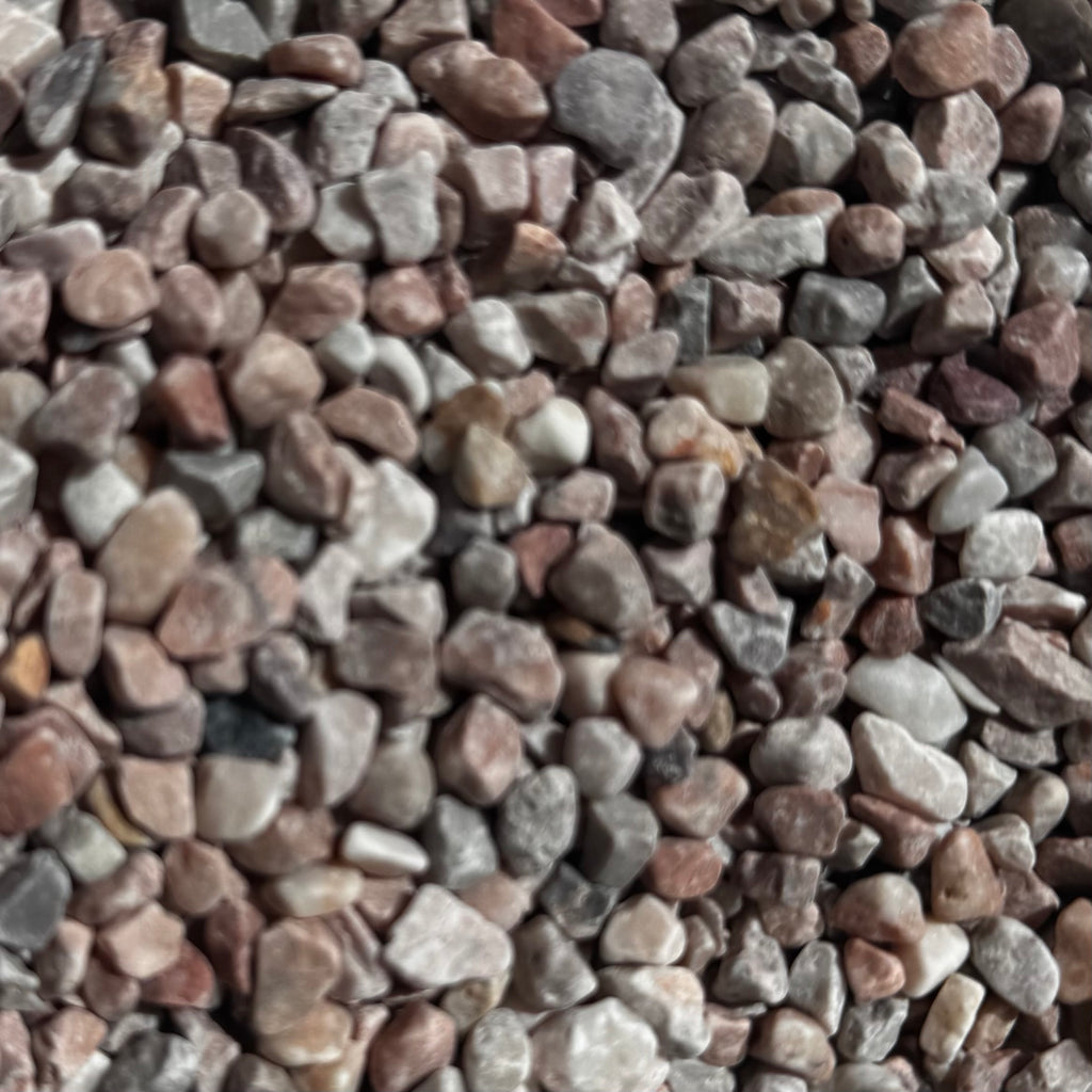 A close-up pile of small decorative pebbles and gravel stones in mixed earthy tones including brown, gray, beige, and muted pink.